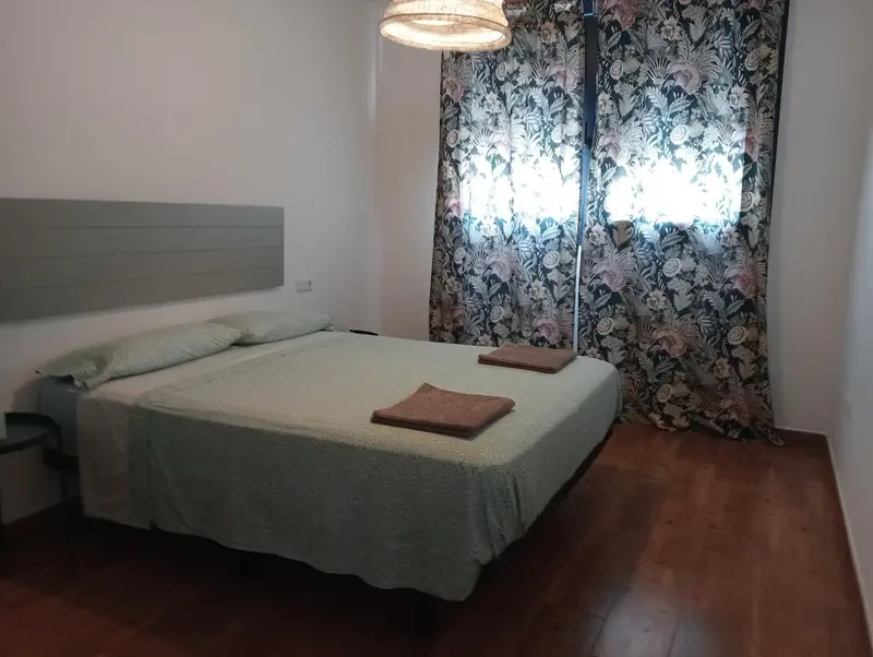 Une chambre lumineuse avec un lit recouvert d'une couverture verte et des rideaux à motifs.