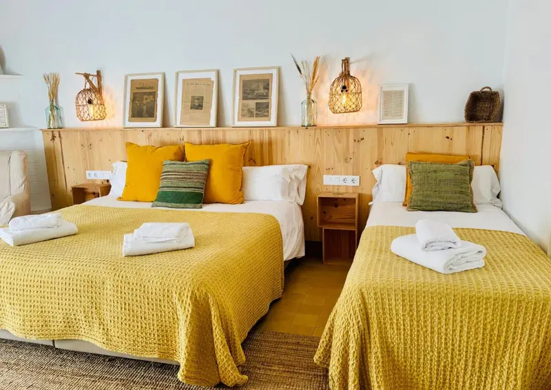 Chambre lumineuse avec deux lits simples et un lit d'une place, décorée de coussins colorés et d'une tête de lit en bois.