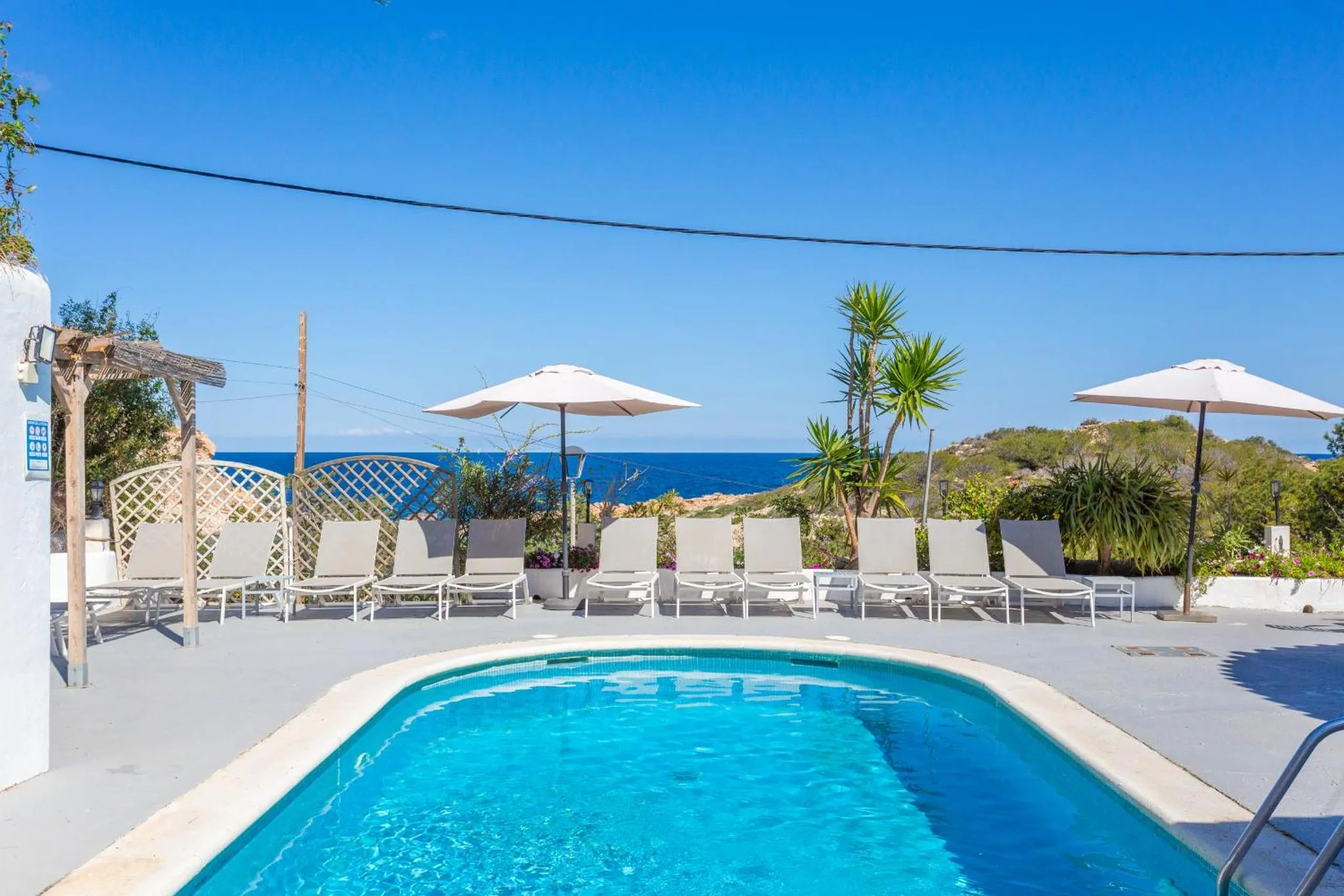 Une piscine rectangulaire avec des transats et des parasols blancs, face à la mer.