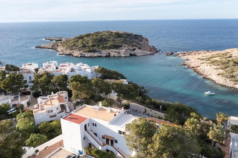Vue aérienne d'une côte rocheuse avec des bâtiments blancs et la mer turquoise.