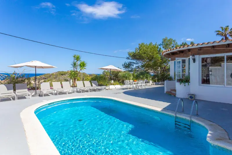 Une piscine rectangulaire avec des transats et parasols, devant un bâtiment blanc.