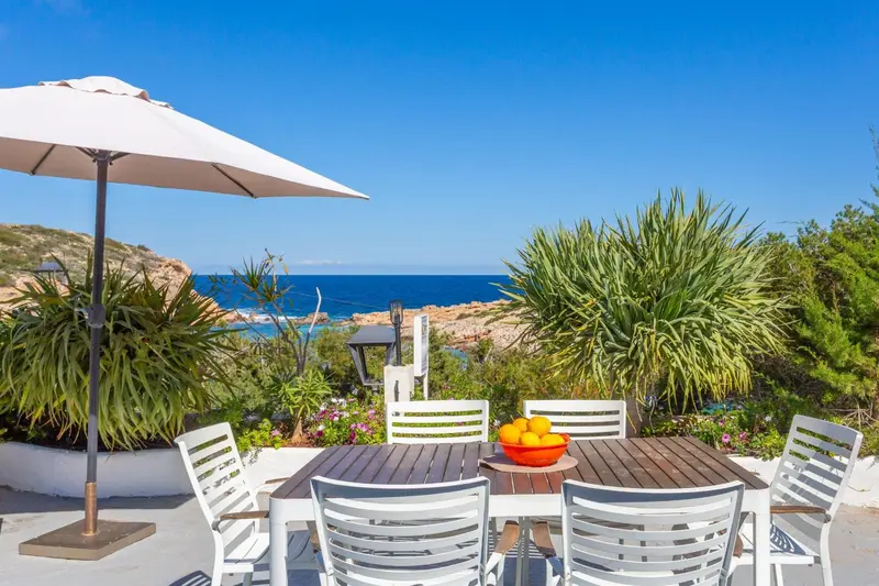 Table et chaises en osier sur une terrasse ensoleillée avec vue sur la mer.