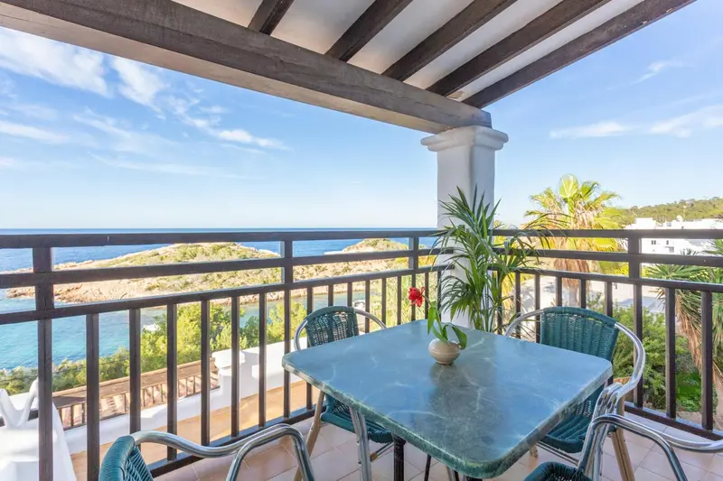 Terrasse avec table et chaises donnant sur la mer et la côte.