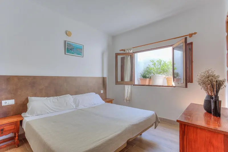 Une chambre lumineuse avec un lit double et une fenêtre ouverte sur la végétation.