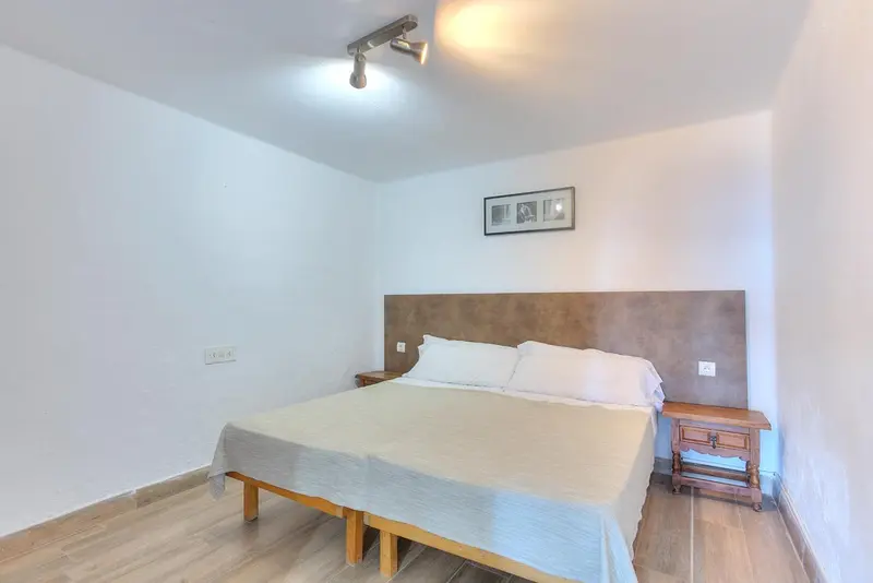 Une chambre lumineuse avec un lit double et une table de chevet en bois.