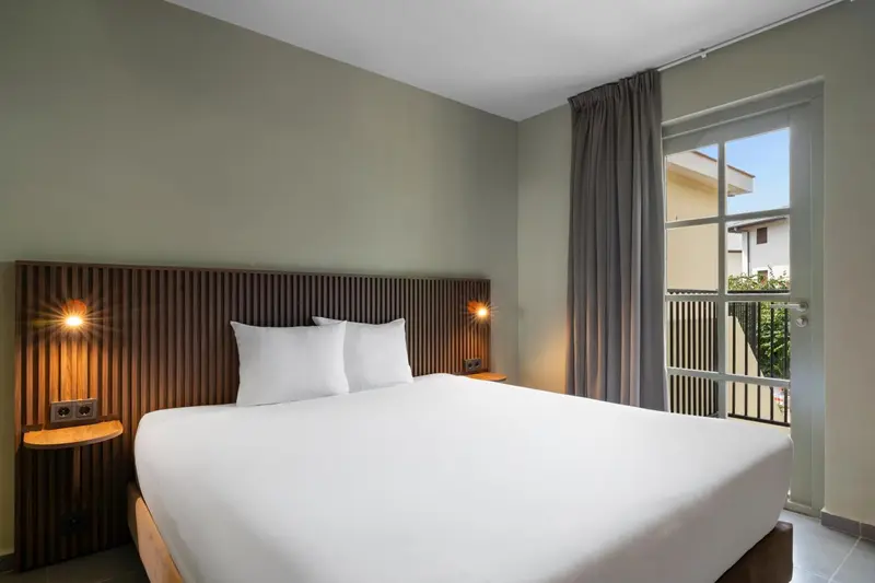Une chambre lumineuse avec un grand lit et un accès à un balcon.