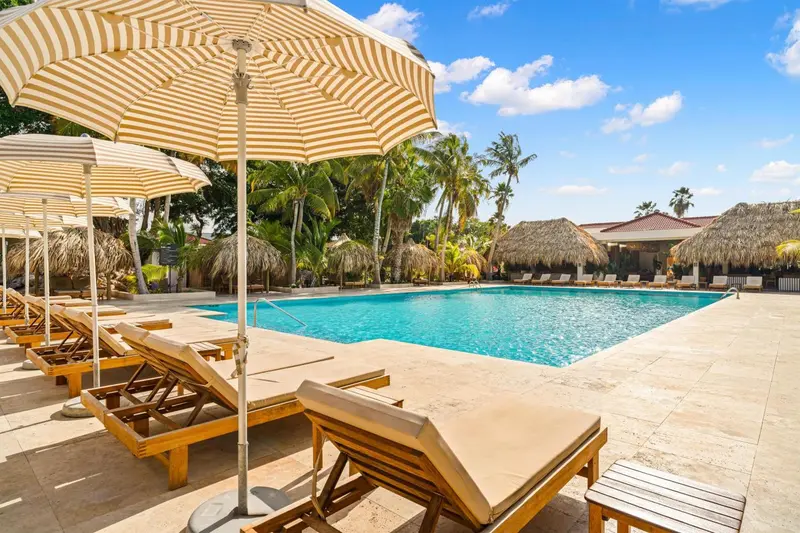 Transats et parasols bordent une piscine turquoise dans un cadre tropical.