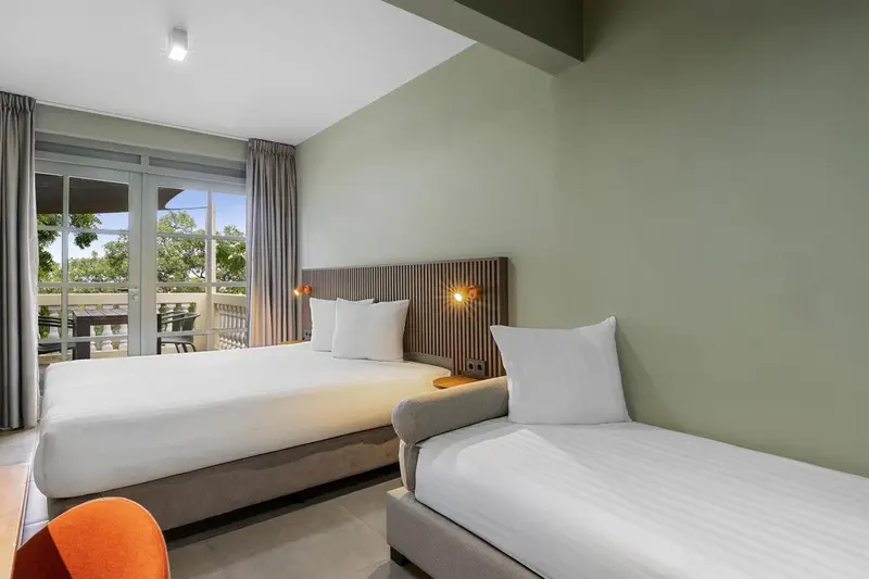 Une chambre lumineuse avec deux lits et une vue sur la végétation.