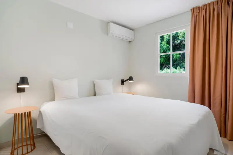 Une chambre lumineuse avec un lit blanc et des rideaux orangés.