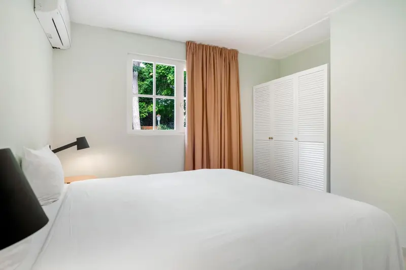 Une chambre lumineuse avec un lit fait et un rideau orangé.