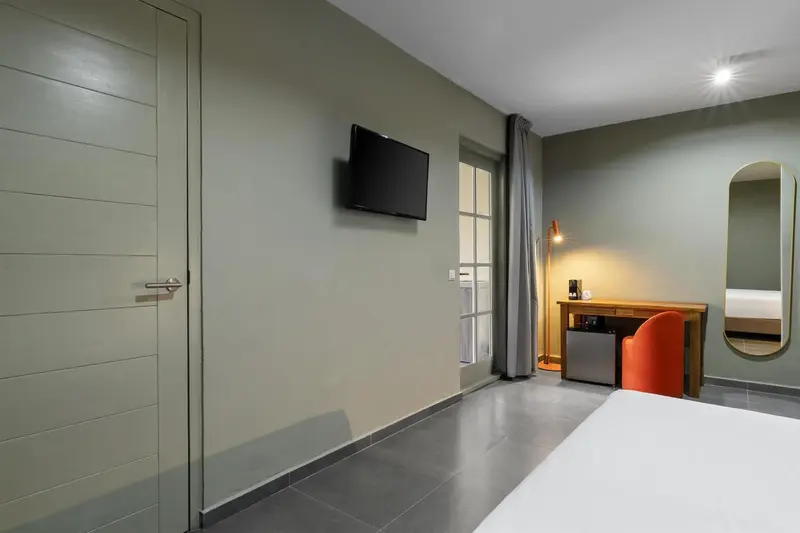 Une chambre lumineuse avec un lit blanc et un téléviseur mural.