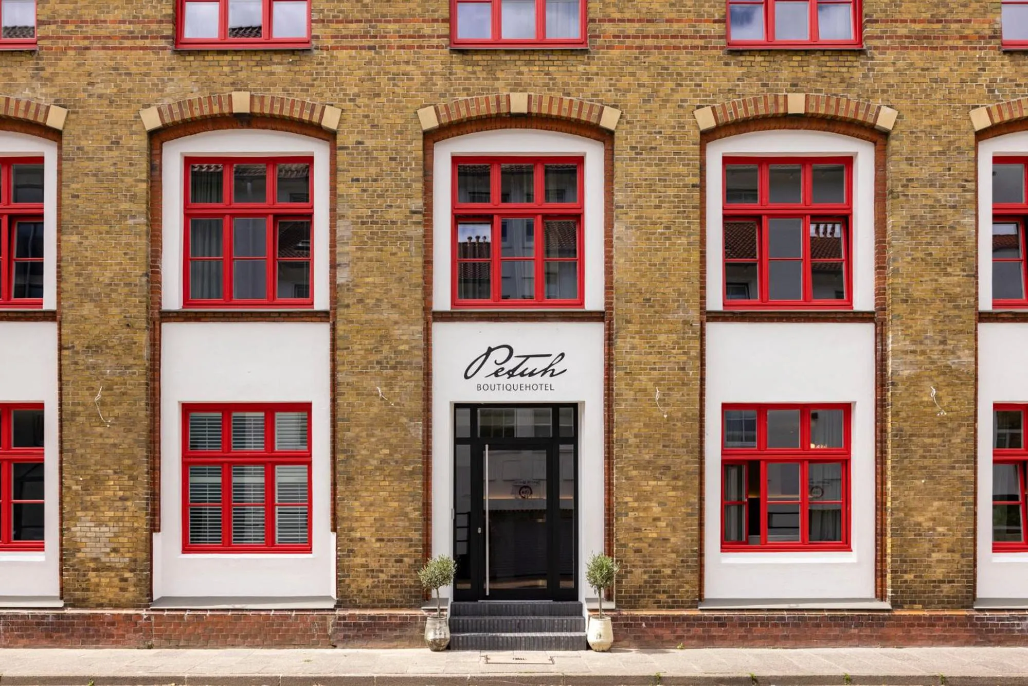 Facade d'un bâtiment en briques avec des fenêtres à encadrement rouge et une entrée sombre.