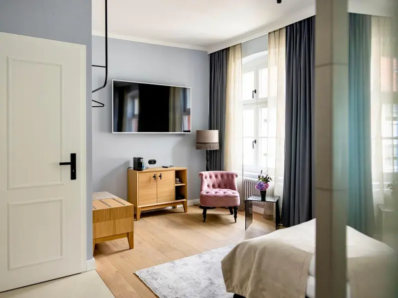 Une chambre lumineuse avec un téléviseur mural et un fauteuil rose.