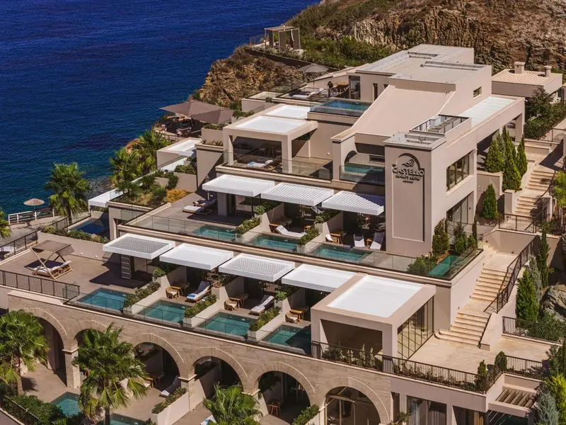 Vue aérienne d'un bâtiment blanc avec des terrasses et des piscines surplombant la mer.