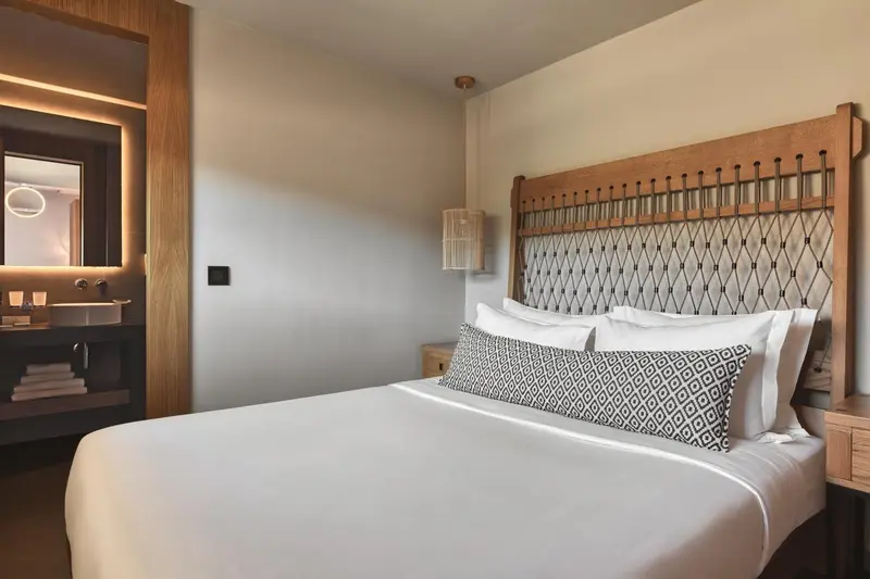 Lit double avec une tête de lit en bois et des oreillers blancs dans une chambre lumineuse.