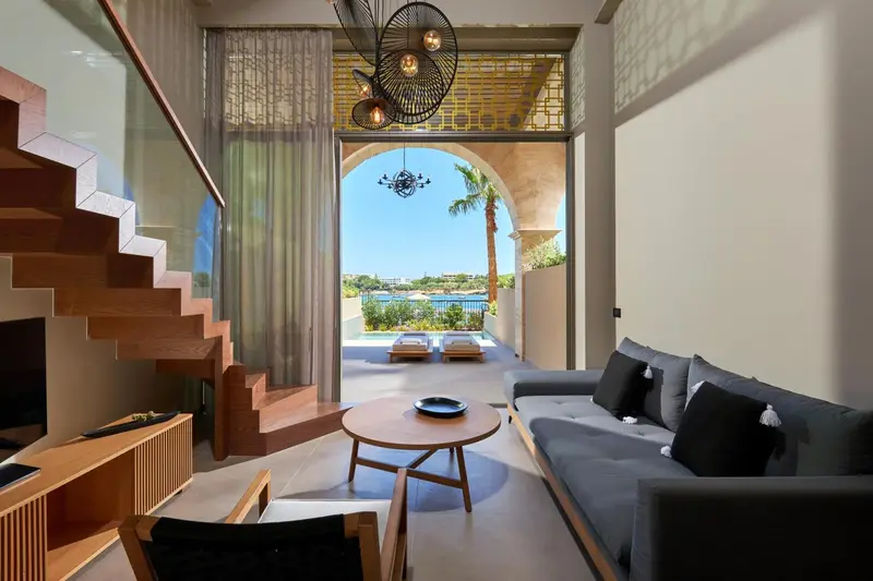 Espace de vie intérieur avec canapé et escalier en bois donnant sur une terrasse.
