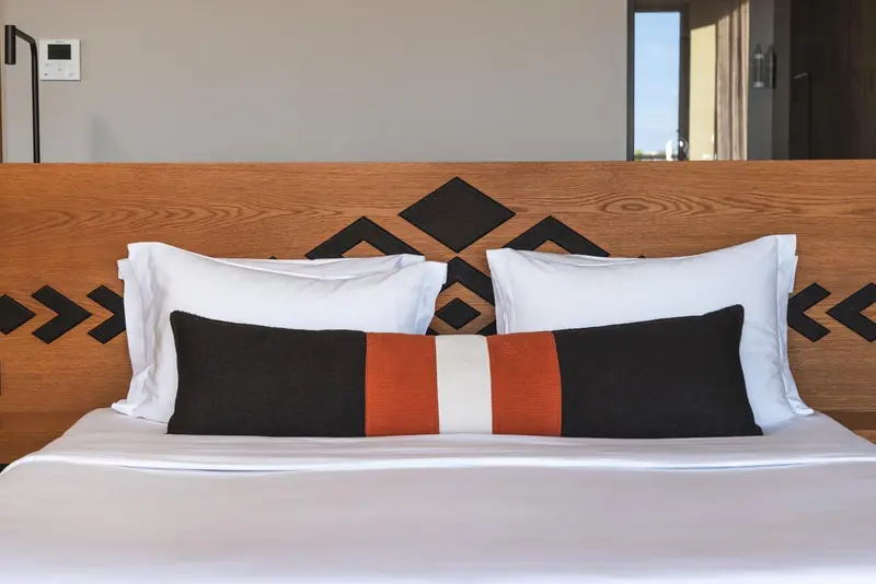 Un lit est fait avec des oreillers blancs et un coussin décoratif.