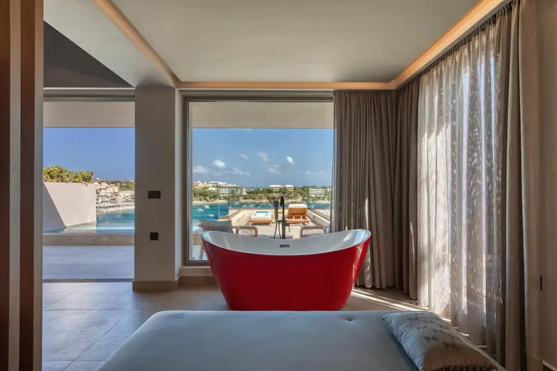 Une baignoire rouge se trouve devant une grande baie vitrée donnant sur la mer.