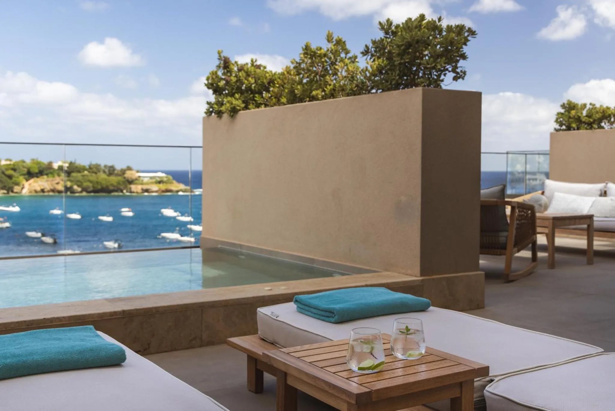 Transats et petite table basse sur une terrasse avec piscine à débordement donnant sur la mer.