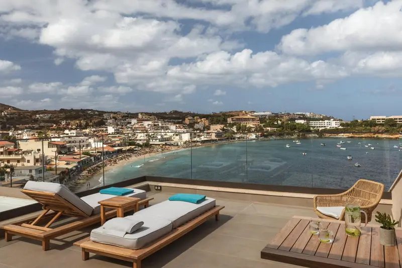Transats et table basse sur une terrasse avec vue sur la mer et la ville.