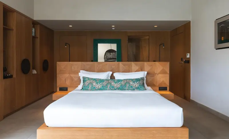 Une chambre lumineuse avec un grand lit recouvert d'une courtepointe blanche et de coussins verts.