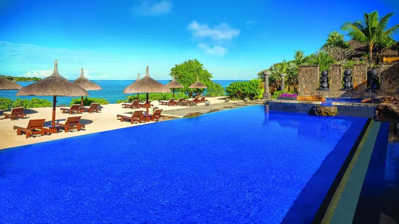 Une piscine à débordement bleu vif surplombe une plage de sable blanc et la mer.