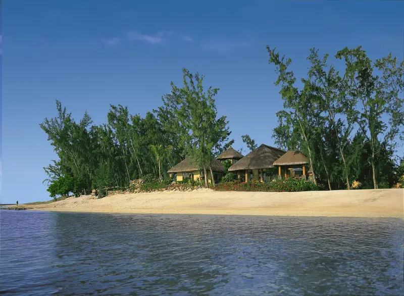 Plage de sable fin bordée de végétation luxuriante et de bungalows aux toits de chaume.