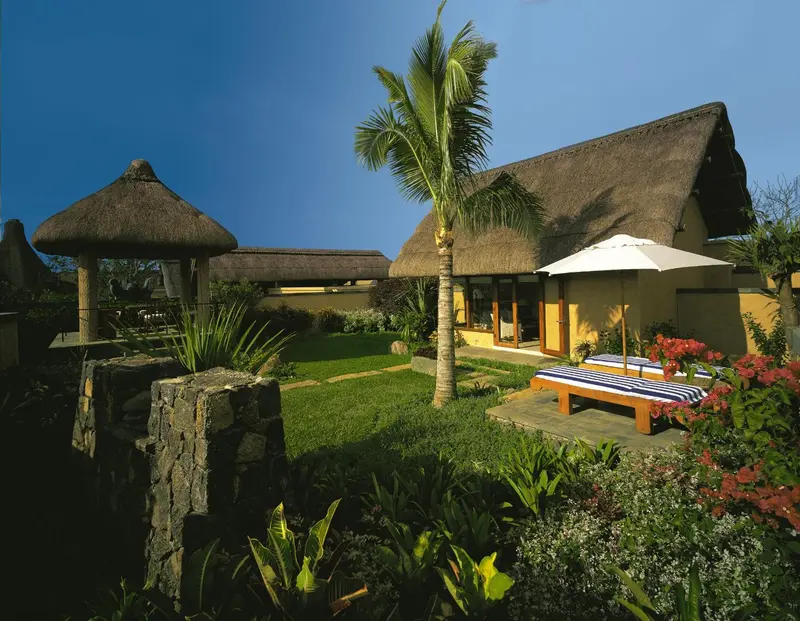 Bâtiment à toit de chaume avec végétation tropicale et mobilier de jardin.