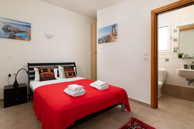 Une chambre lumineuse avec un lit recouvert d'une courtepointe rouge et une salle de bain attenante.