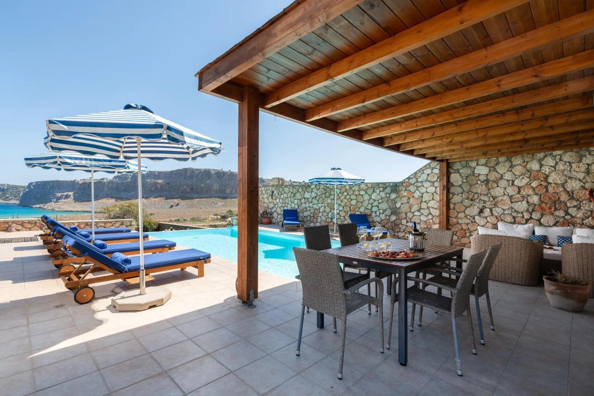 Terrasse ombragée avec table à manger et chaises, donnant sur une piscine et la mer.