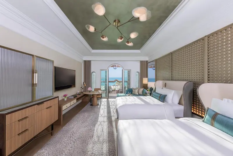 Chambre lumineuse avec deux lits et vue sur la mer par une baie vitrée.