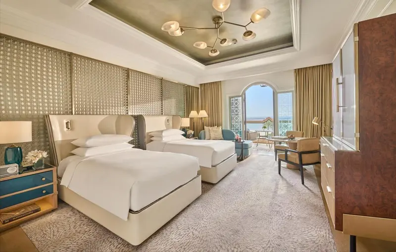 Chambre lumineuse avec deux lits simples et un coin salon près d'une fenêtre.