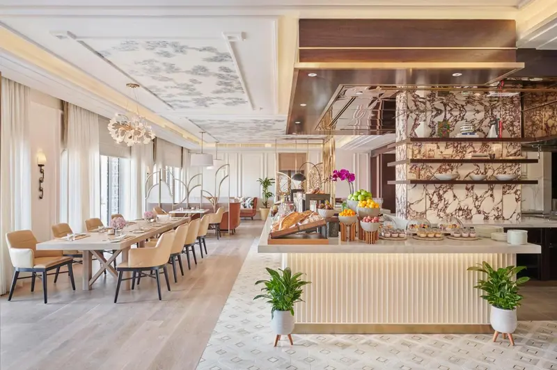 Une salle lumineuse avec des tables dressées et un buffet garni de fruits et de pâtisseries.