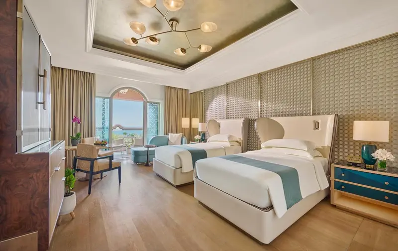 Chambre lumineuse avec deux lits simples et vue sur la mer.