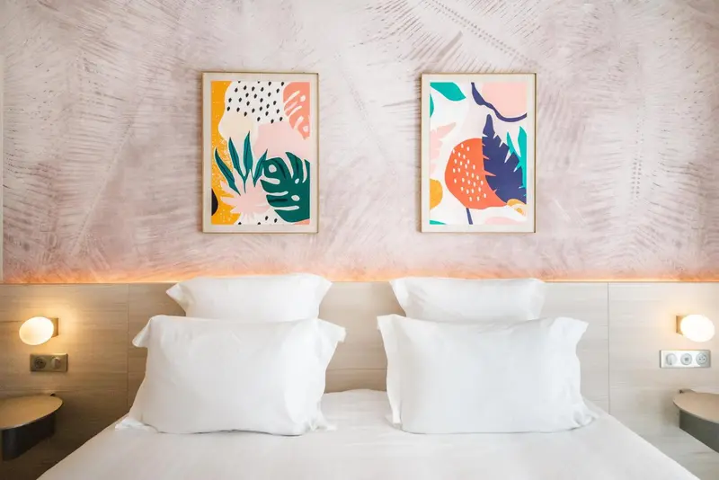 Un lit double blanc avec des oreillers moelleux dans une chambre décorée de tableaux colorés.