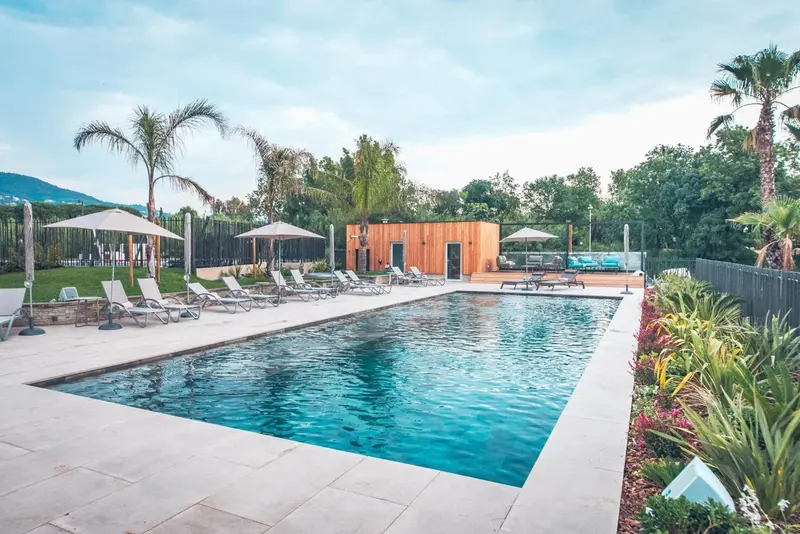 Une piscine rectangulaire bordée de chaises longues et de parasols, entourée d'une végétation luxuriante.