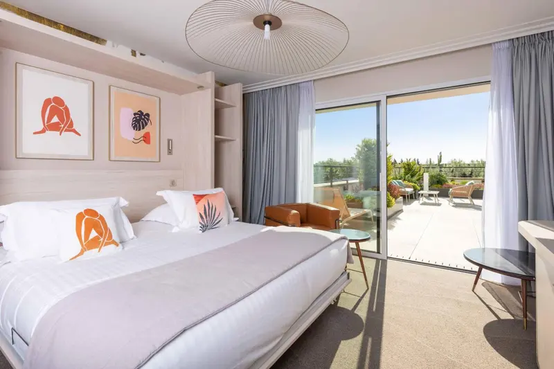 Chambre lumineuse avec un grand lit et une vue sur une terrasse ensoleillée.
