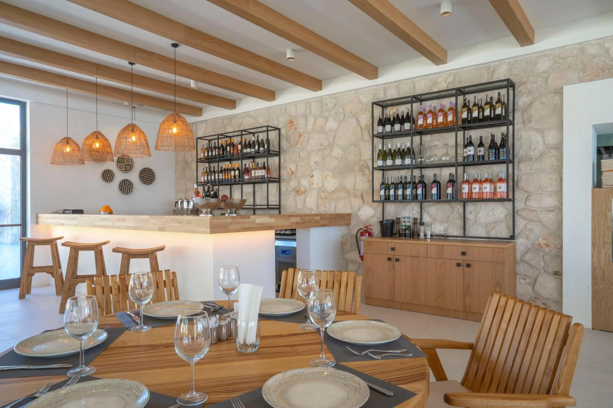 Une table est dressée dans une salle lumineuse avec un comptoir et des étagères à vin.
