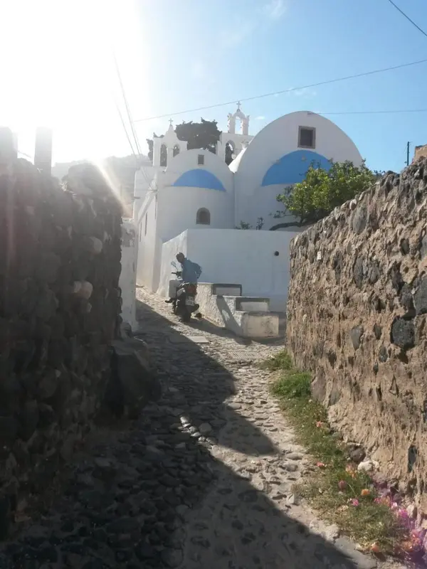 Une ruelle pavée mène vers des bâtiments blancs aux dômes bleus sous un ciel ensoleillé.