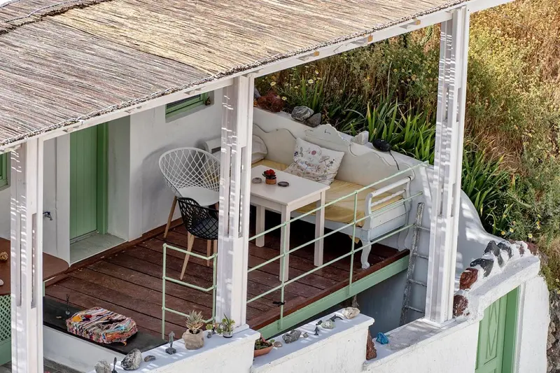 Petite terrasse avec table et chaises en fer forgé, décorée de plantes et de coussins.