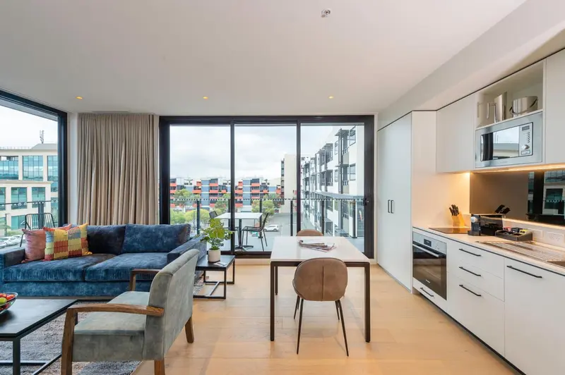 Espace de vie lumineux avec canapé bleu et cuisine équipée donnant sur une vue urbaine.