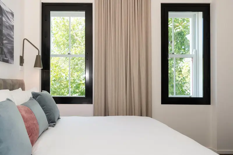 Une chambre lumineuse avec un grand lit et deux fenêtres.