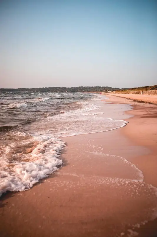 Vague déferlant sur une plage de sable fin au coucher du soleil.