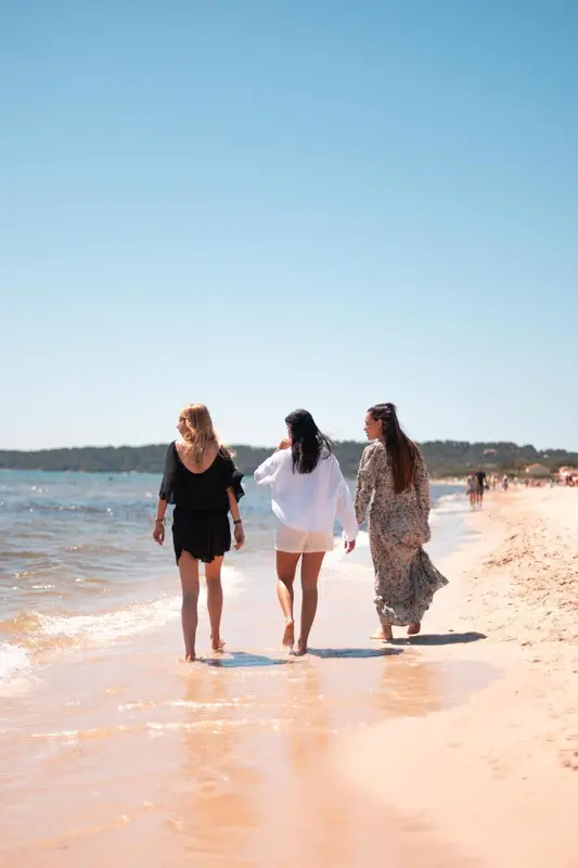 Trois femmes marchent sur une plage de sable fin, face à la mer.