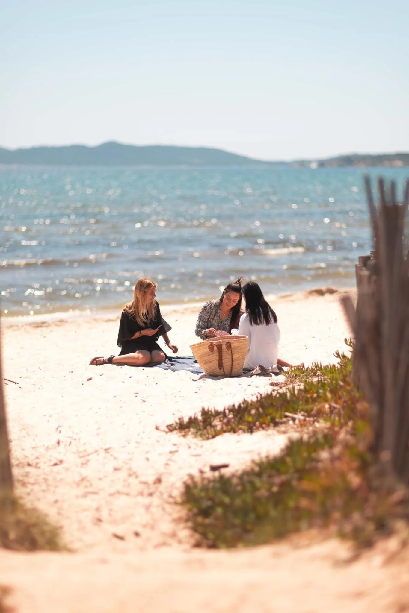 Trois personnes assises sur le sable fin d'une plage ensoleillée, face à la mer.