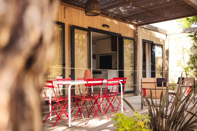 Terrasse avec table et chaises rouges devant une ouverture sur un espace intérieur.