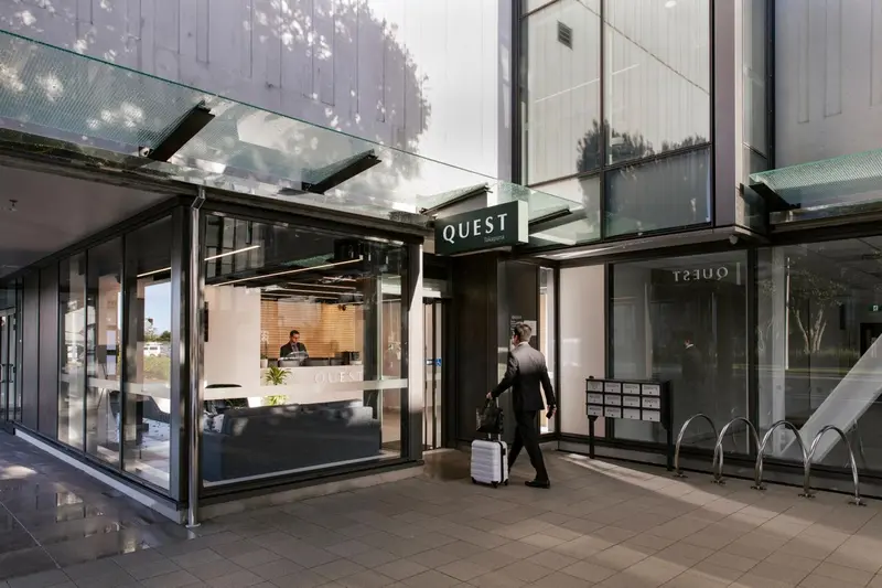 Façade d'un bâtiment avec une entrée vitrée et un homme tirant une valise.