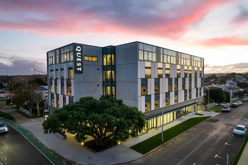 Bâtiment moderne à plusieurs étages avec un ciel rose au coucher du soleil.