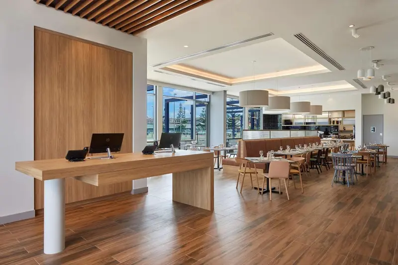Un comptoir d'accueil en bois clair dans un espace lumineux avec des tables et des chaises.