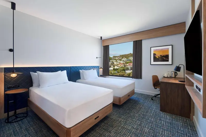 Chambre moderne avec deux lits simples et vue sur la ville.